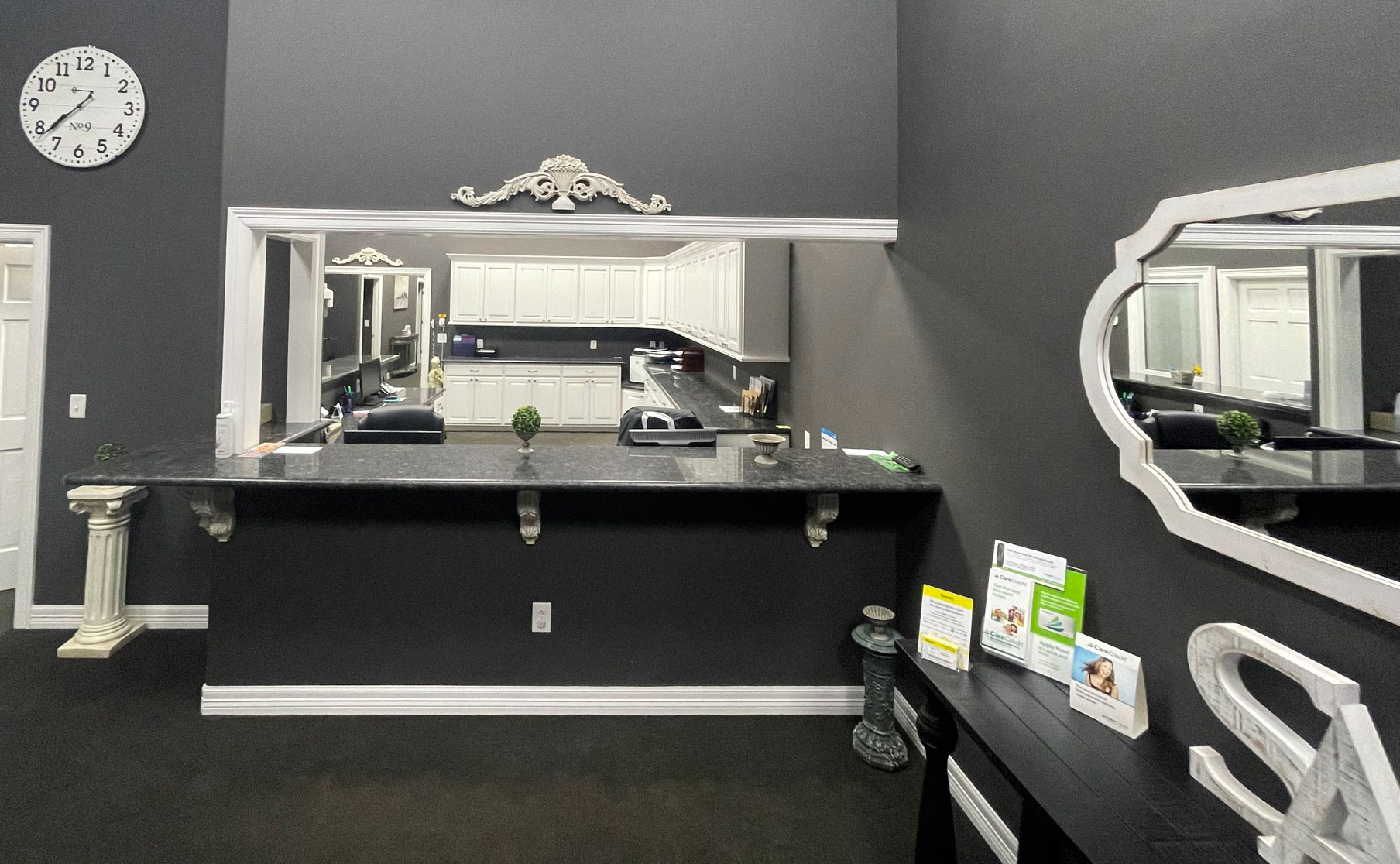 The image shows a well-lit, modern hair salon interior with a dark wall and a large mirror reflecting the room.