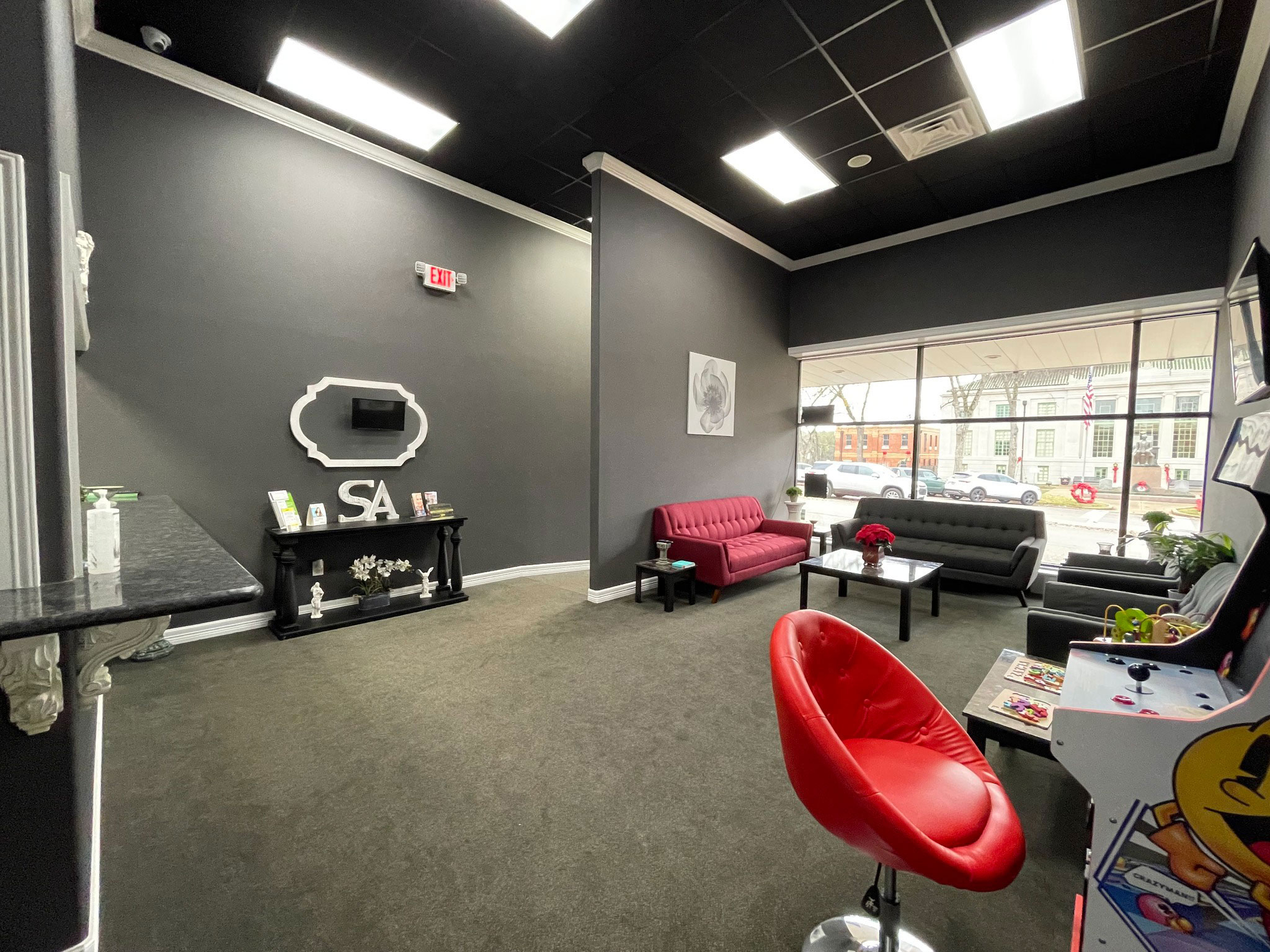 The image is a photograph of an interior space that appears to be a gaming or entertainment room with a red sofa, a video game console, and a black carpeted floor.