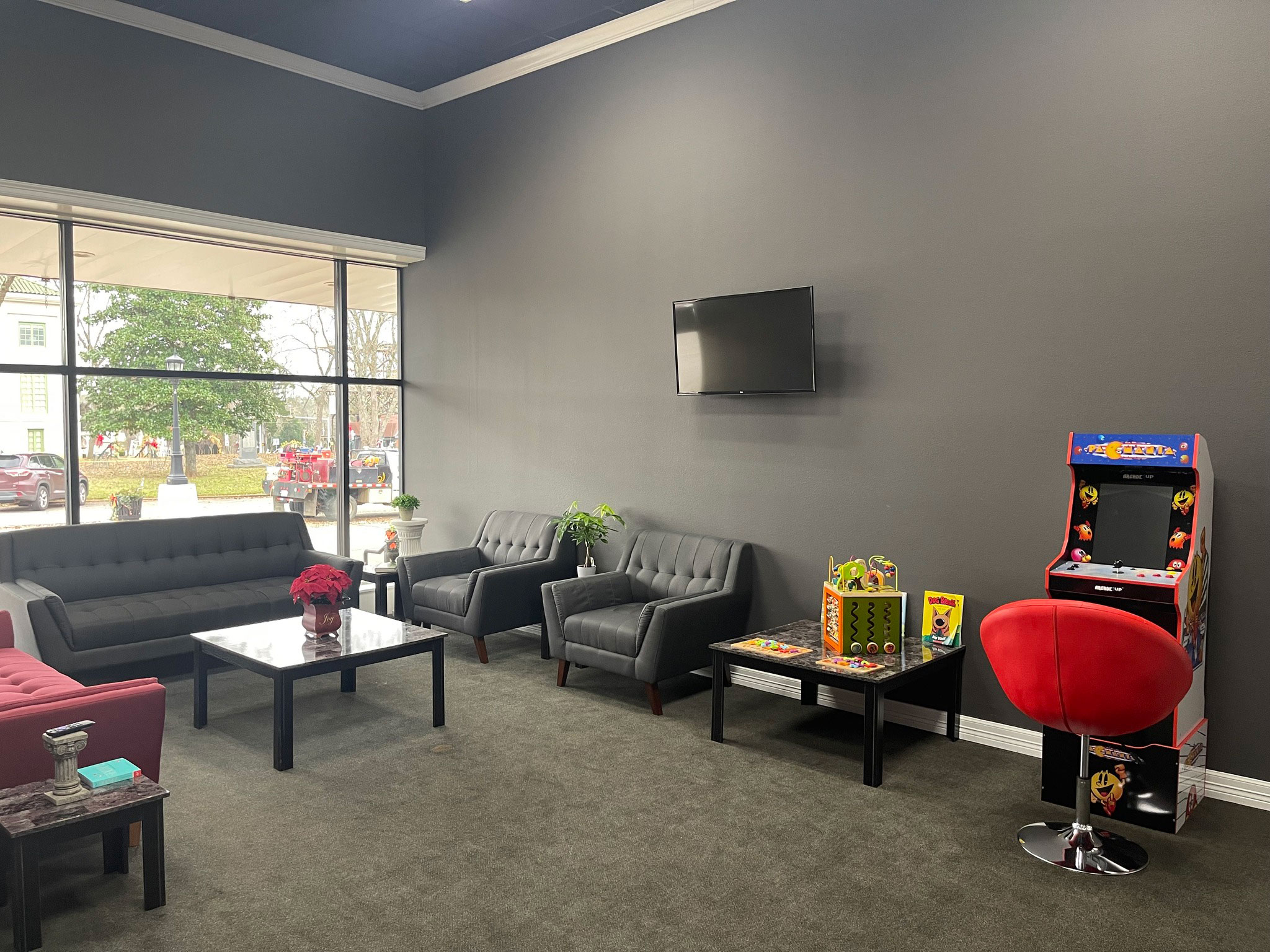 A well-lit lobby with a modern furniture arrangement, featuring a red sofa, a black coffee table, and a gaming area with a TV and video games.