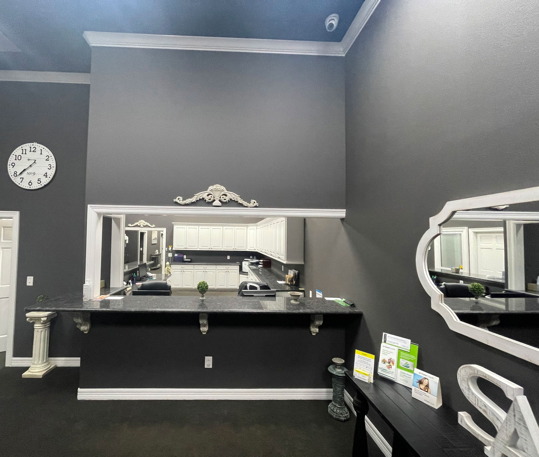 The image shows an interior space, likely a salon or barber shop, featuring a large mirror on the wall above a counter with a sink and vanity. The room is decorated in a monochromatic color scheme, predominantly black and white, with a modern design.