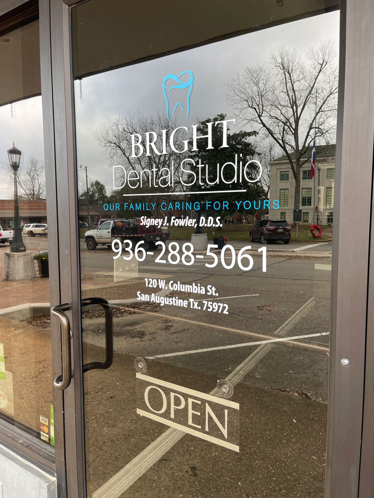 The image shows a storefront window of a dental studio named 'Bright Dental Studio.' There is an open sign in the window, and the text on the sign includes a phone number.