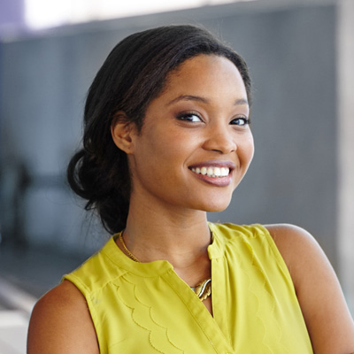 The image shows a woman with a radiant smile, posing for the camera. She is wearing a yellow top and has dark hair styled in an updo.