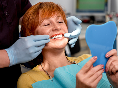 A woman in a dental chair receiving oral care, with a blue mouthguard and a smile.