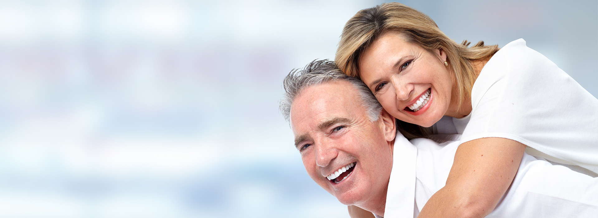 The image shows a man and woman, presumably an older couple, smiling and embracing each other in front of a blurred background.