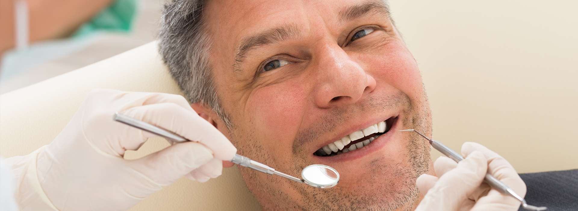 A man sitting in a dental chair, receiving dental treatment with tools and instruments visible around him.