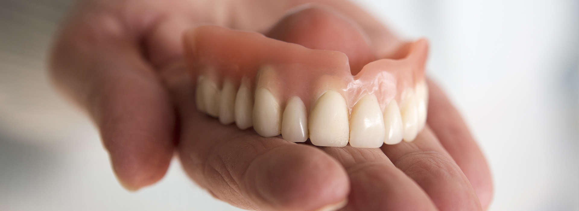 This image depicts a human hand holding a set of artificial teeth, showcasing the dentures with a focus on their dental structure and appearance.