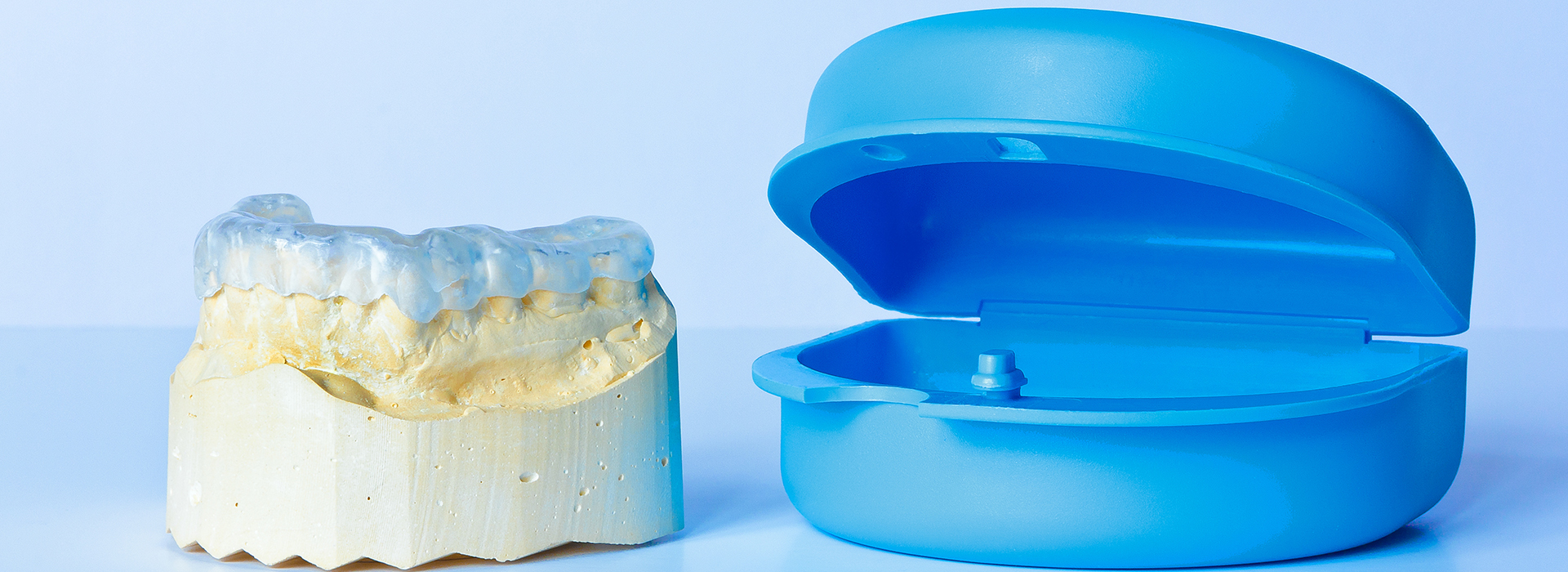 The image shows a blue plastic toothbrush and a yellow plastic toothpaste tube, placed side by side against a white background.