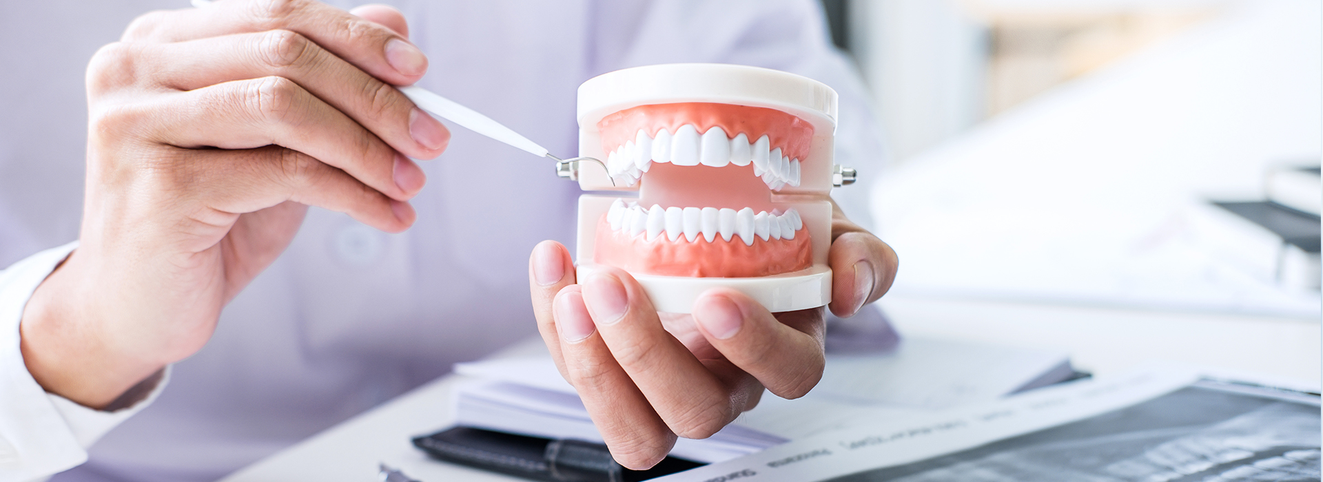 A person s hand holding a coffee cup with a white smiley face, while another hand is holding a toothbrush and toothpaste. The background shows an office setting with a desk and computer monitor.