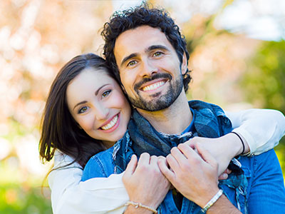 A man and a woman embracing, both smiling, with the man wearing a scarf around his neck.