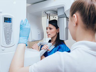 The image shows a woman in a blue uniform standing next to a large, modern 3D scanner machine, with another person looking at it from behind.