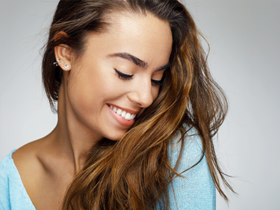 A young woman with long hair, wearing a light blue top, smiling at the camera.