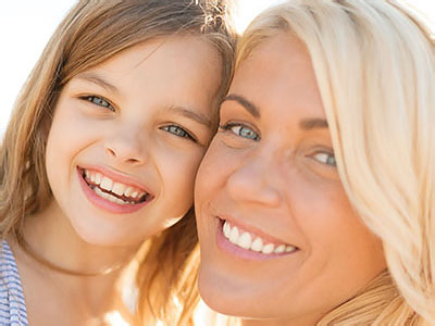 A woman and a young girl smiling at the camera, with the woman s face partially obscured by the child.