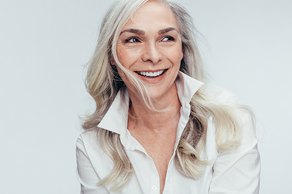 A smiling woman with short hair, wearing a white shirt and a blazer, against a light background.