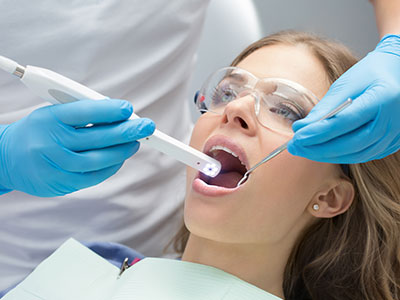 A woman receiving dental care, with a dental hygienist operating an ultrasonic cleaning device.