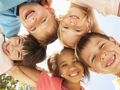 A group of children, possibly siblings, smiling together in a sunny outdoor setting.