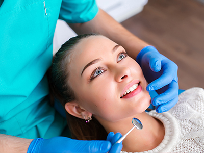 The image shows a woman in a dental chair receiving treatment from a dentist, with the focus on her smiling face and the dental tools being used.